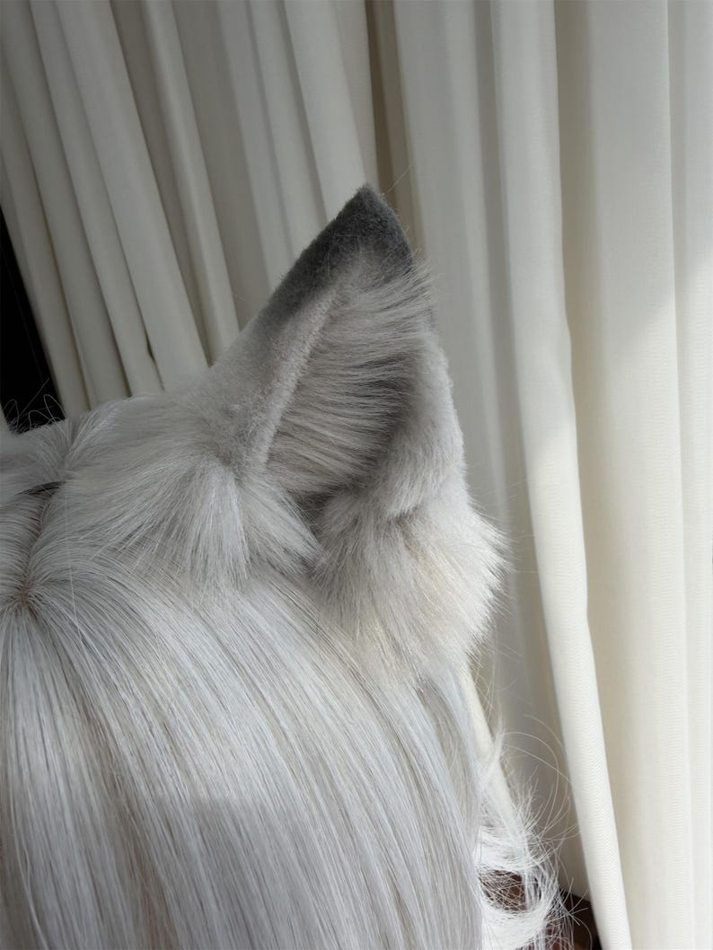 Puede incluir: Un par de orejas de lobo de piel sint&eacute;tica gris y blanca unidas a una peluca. Las orejas son de color gris claro con puntas grises m&aacute;s oscuras. La peluca tiene pelo largo, liso y gris claro.