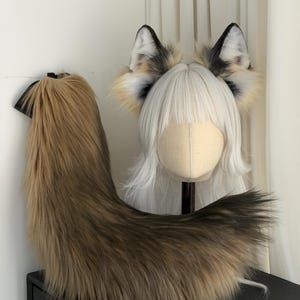 May include: A faux fur fox tail and headband with ears. The tail is brown and black, and the ears are white, black, and tan. The headband has a white wig attached to it.