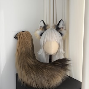 May include: A faux fur fox tail and ear set. The tail is brown and tan, with a black ribbon attachment. The ears are white, black, and tan, attached to a wig head with white hair. The set is designed for cosplay or costume use.