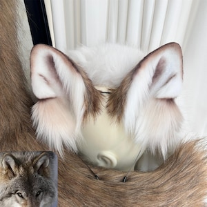 May include: Faux fur wolf ears in white and brown tones, attached to a headband. The image also shows a section of a faux fur tail. The ears are designed to be worn as part of a costume or accessory.