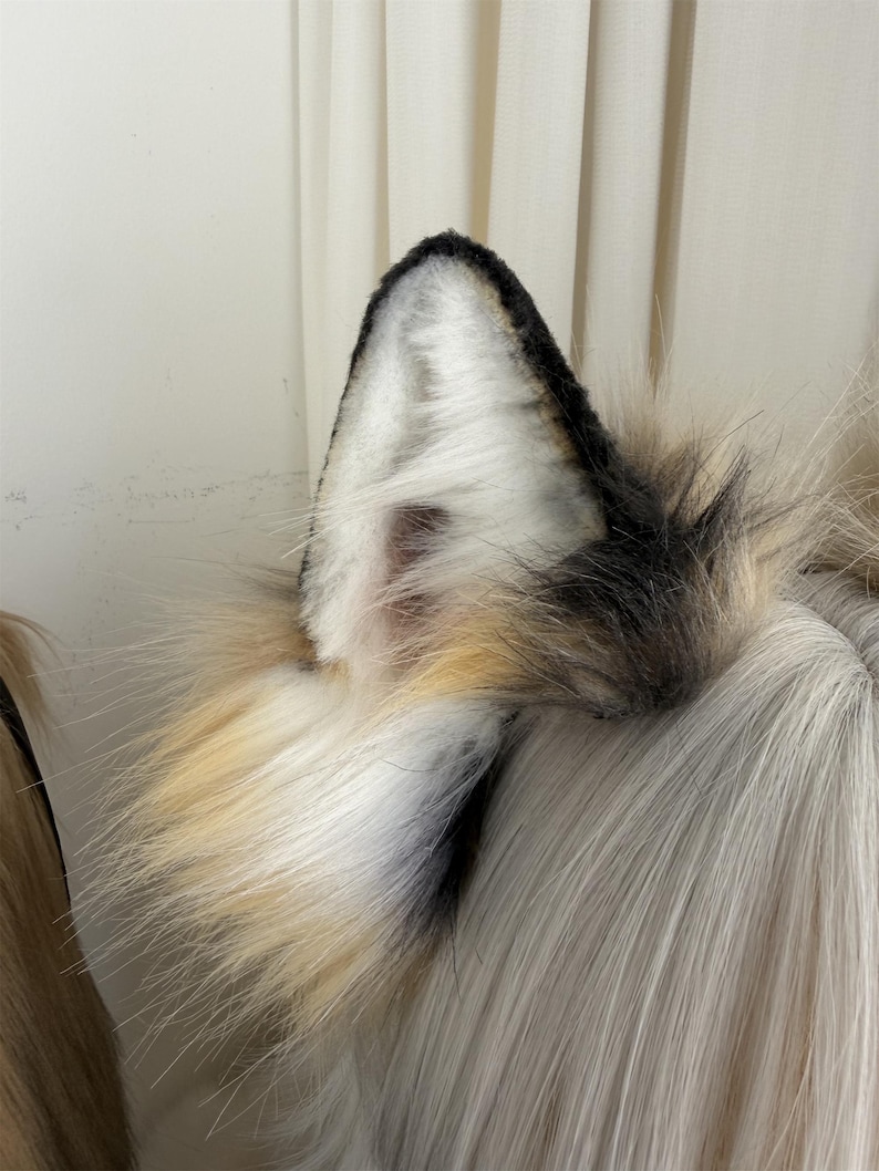 May include: A pair of faux fur wolf ears in black, white, and tan. The ears are attached to a light-colored wig. The ears have a realistic design with a black tip and a white interior.
