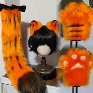 May include: A cosplay set featuring a long, orange and black striped tail with a black bow, a wig with orange and black cat ears, and two orange paw-shaped hand covers. The set is designed to resemble a tiger.