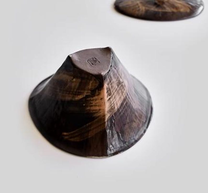 Pu&ograve; includere: Una ciotola in ceramica marrone scuro con un design testurizzato che ricorda le pennellate. La ciotola ha una forma angolare unica e un piccolo segno quadrato all'interno.