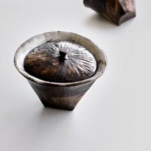 Pu&ograve; includere: Una ciotola in ceramica bianca e nera con un coperchio. La ciotola ha un design testurizzato, organico e un bordo leggermente svasato. Il coperchio si adatta perfettamente alla parte superiore della ciotola.