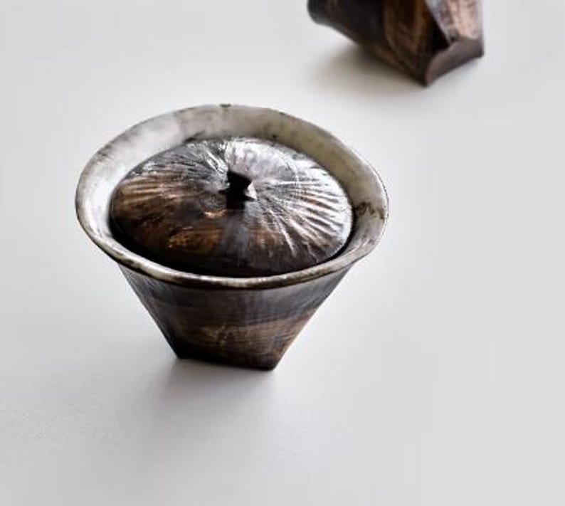 Pu&ograve; includere: Una ciotola in ceramica bianca e nera con un coperchio. La ciotola ha un design testurizzato, organico e un bordo leggermente svasato. Il coperchio si adatta perfettamente alla parte superiore della ciotola.