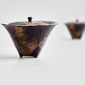 Pu&ograve; includere: Una tazza da t&egrave; in ceramica marrone con un coperchio e tre gambe. La tazza da t&egrave; ha un design testurizzato, simile a pennellate.