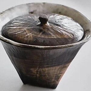 Pu&ograve; includere: Un contenitore in ceramica con coperchio, con una smaltatura marrone scuro con striature bianche e una superficie testurizzata.
