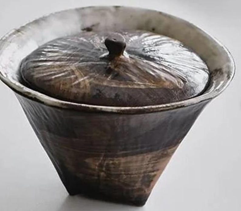 Pu&ograve; includere: Un contenitore in ceramica con coperchio, con una smaltatura marrone scuro con striature bianche e una superficie testurizzata.
