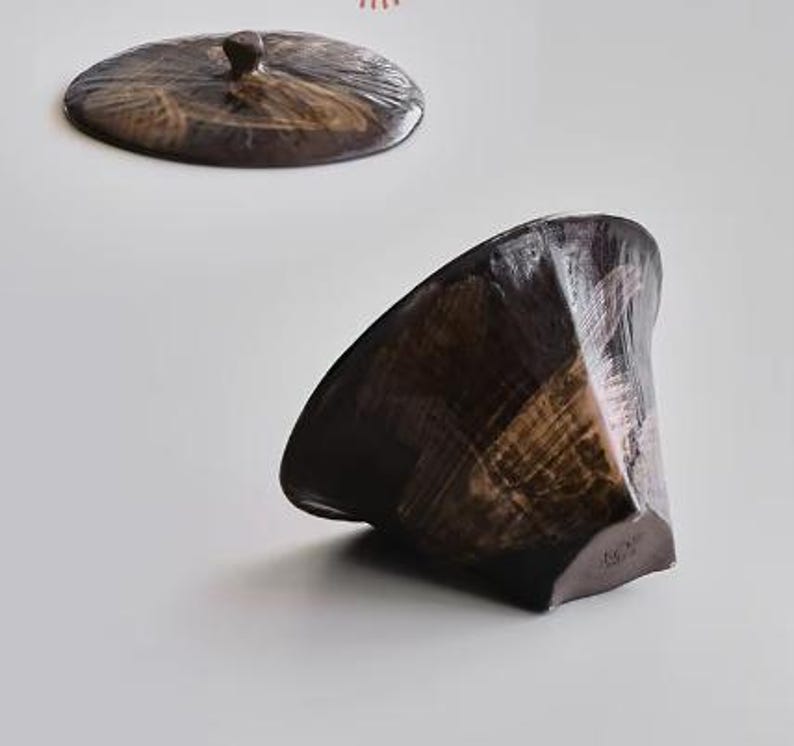 Pu&ograve; includere: Una ciotola in ceramica marrone scuro con un design geometrico testurizzato. La ciotola ha un'apertura larga e svasata e una base stretta. La ciotola &egrave; realizzata in argilla marrone scuro e ha una finitura lucida.