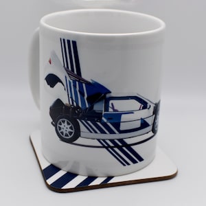 以下が含まれることがあります： 白地に青と白のスポーツカーのグラフィックが描かれた白いセラミックマグカップ。マグカップは青と白のコースターの上に置かれています。