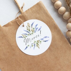 May include: A white round gift tag with a watercolor illustration of lavender flowers and the word "Merci!" in black calligraphy.