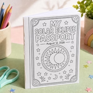 Könnte beinhalten: Ein weißes Heft mit schwarzer Strichzeichnung auf dem Einband, das den Text MY SOLAR ECLIPSE PASSPORT und das Datum August 12, 2026 zeigt. Das Design enthält eine zentrale Sonnen- und Mondgrafik, umgeben von Sternen und Bordüren.