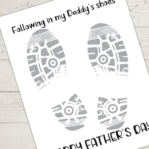 Pu&ograve; includere: Un biglietto bianco per la festa del pap&agrave; con illustrazioni di impronte di scarpe grigie. Il testo recita "Following in my Daddy's shoes" e "Happy Father's Day" in nero. Il biglietto &egrave; su una superficie di legno chiaro.