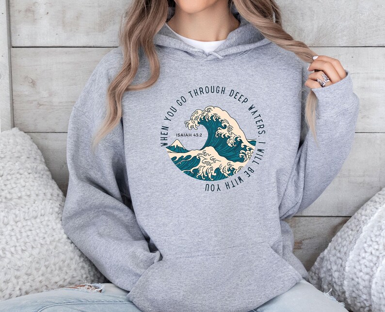 K&ouml;nnte beinhalten: Grauer Kapuzenpullover mit einem Grafikdruck einer blauen Welle und dem Text "When you go through deep waters, I will be with you. Isaiah 43:2"