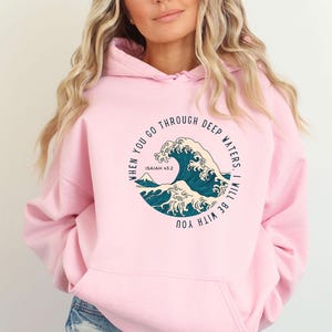 K&ouml;nnte beinhalten: Rosafarbener Hoodie mit einem Grafikdruck einer blauen Welle und dem Text "When you go through deep waters. I will be with you. Isaiah 43:2"