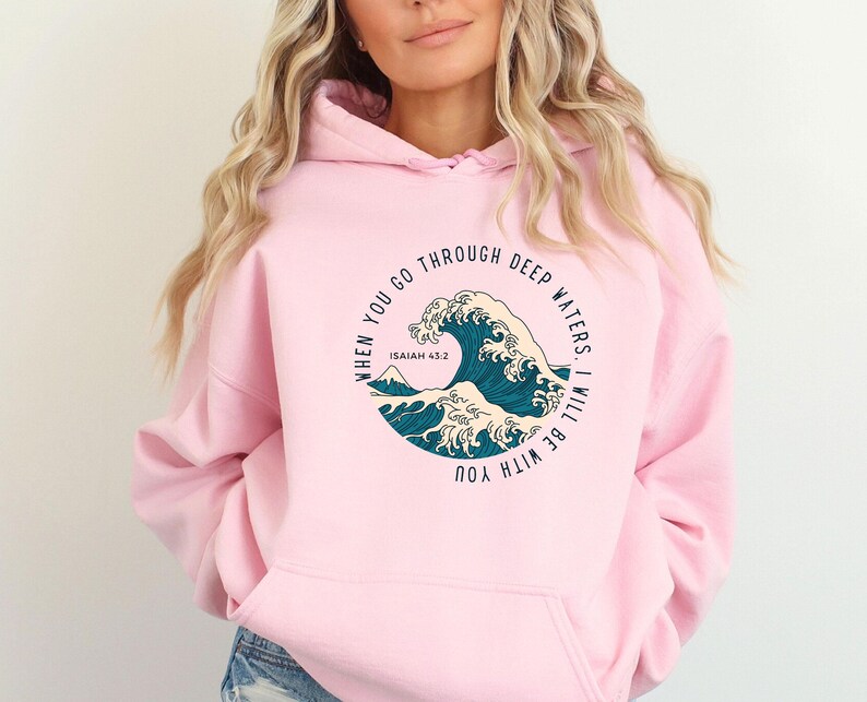K&ouml;nnte beinhalten: Rosafarbener Hoodie mit einem Grafikdruck einer blauen Welle und dem Text "When you go through deep waters. I will be with you. Isaiah 43:2"