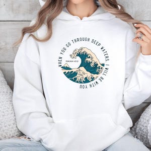 K&ouml;nnte beinhalten: Wei&szlig;er Hoodie mit einem blauen und wei&szlig;en Wellendesign und dem Text "When you go through deep waters. I will be with you. Isaiah 43:2"