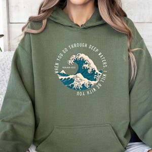 K&ouml;nnte beinhalten: Ein gr&uuml;ner Kapuzenpullover mit einem grafischen Aufdruck einer Welle und dem Text "WHEN YOU GO THROUGH DEEP WATERS, I WILL BE WITH YOU" und "ISAIAH 43.2".