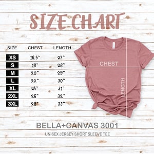May include: Size chart for a unisex jersey short sleeve tee, showing chest and length measurements in inches for sizes XS to 3XL. The chart is on a woodgrain background with a pink t-shirt laid out on top.
