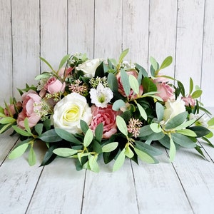May include: A floral arrangement featuring pink and white roses, white flowers, and green foliage. The arrangement is ideal for a wedding, party, or special occasion.