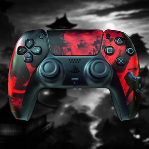 May include: A black and red PlayStation 5 controller with a custom design. The controller features a black base with red accents and a graphic design on the front. The background is a blurred image of a Japanese landscape.