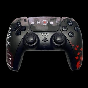 Peut inclure: Manette noire PlayStation 5 avec un design Ghost of Tsushima. Le dessus présente le logo du jeu et un motif de ciel nuageux. Des feuilles d'érable rouges ornent le côté droit, et des caractères japonais sont à gauche.