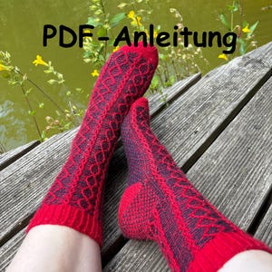Könnte beinhalten: Ein Paar rot-dunkelviolette Strickstrümpfe mit Rautenmuster. Die Socken werden auf einer Holzoberfläche mit dem Text "PDF-Anleitung" in Schwarz dargestellt.