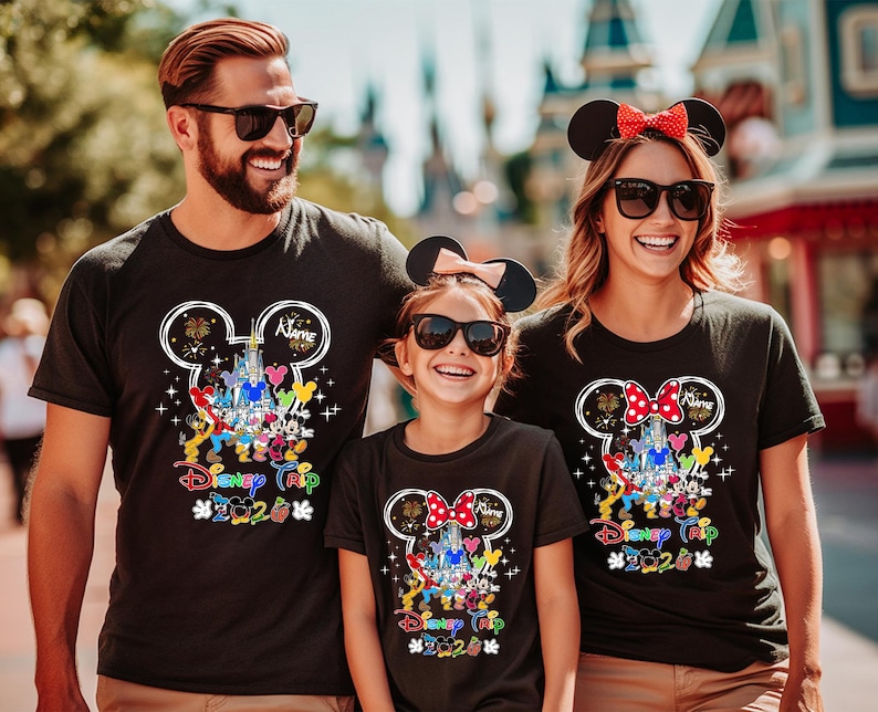 May include: Three people wearing black t-shirts with a Disney theme. The shirts feature a Mickey Mouse head outline with a castle, characters, and the text "Disney Trip 2020". The family is smiling and wearing sunglasses.