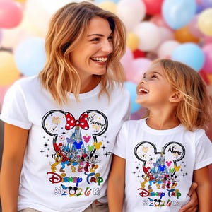 K&ouml;nnte beinhalten: Wei&szlig;e T-Shirts mit Disney-Motiv. Eines hat "Mommy" in einem Minnie-Mouse-Design, das andere "Name". Beide zeigen ein Schloss, Feuerwerk und Disney-Figuren mit dem Text "Disney Trip 2020".