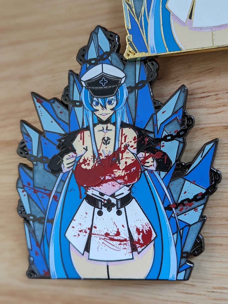 May include: A blue and white enamel pin featuring a female anime character with long blue hair, wearing a white and black military uniform with a red cross on the collar. The character is surrounded by blue ice crystals and chains. The character is covered in red blood splatters.