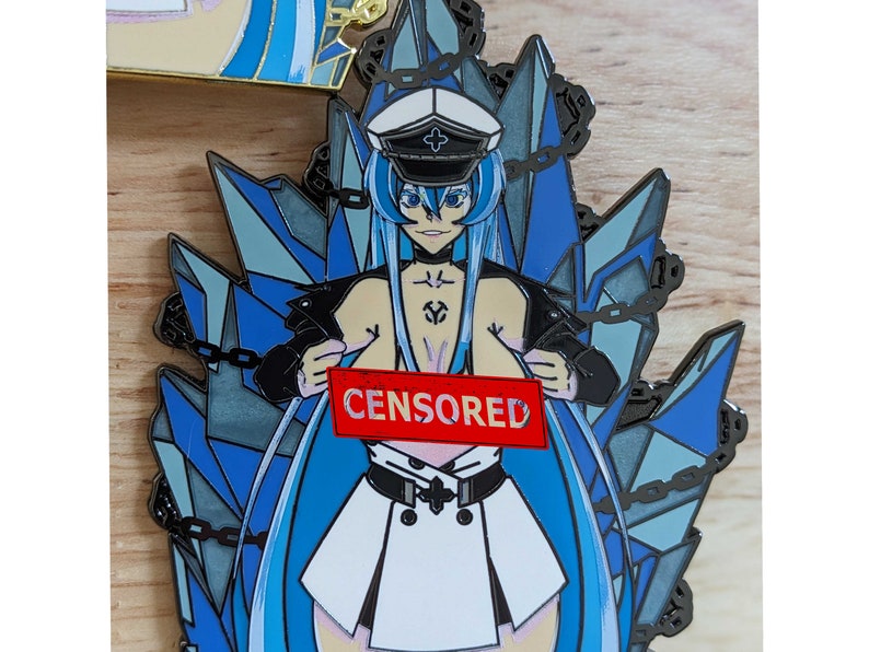 May include: A blue and silver enamel pin featuring an anime character with long blue hair, a white dress, and a black jacket. The character is holding a red sign that says "CENSORED".