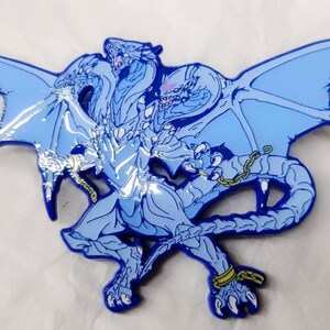 May include: A blue enamel pin depicting a three-headed dragon with chains around its legs and wings. The dragon is standing with its wings outstretched.