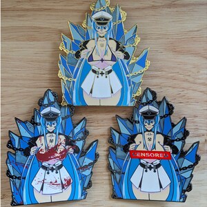 May include: Three enamel pins featuring an anime character with blue hair and a white sailor uniform. The character is surrounded by blue and silver crystals and chains. The pins are in different color variations: gold, black, and red.