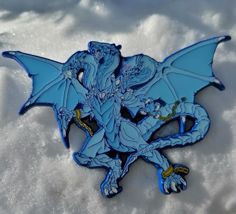 May include: A blue enamel pin depicting a three-headed dragon with wings outstretched. The dragon is shown in a fighting pose with its claws extended.