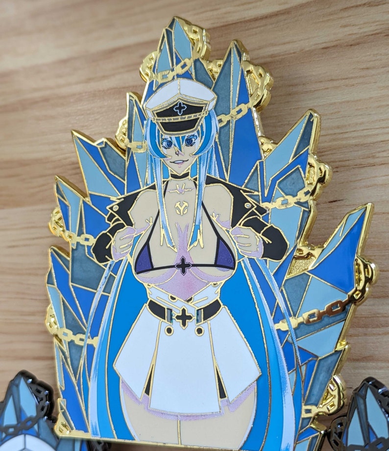 May include: A blue and gold enamel pin featuring a female character with long blue hair, wearing a white and gold sailor hat, a white and gold jacket, and a white skirt. The character is sitting on a throne made of blue and gold crystals.