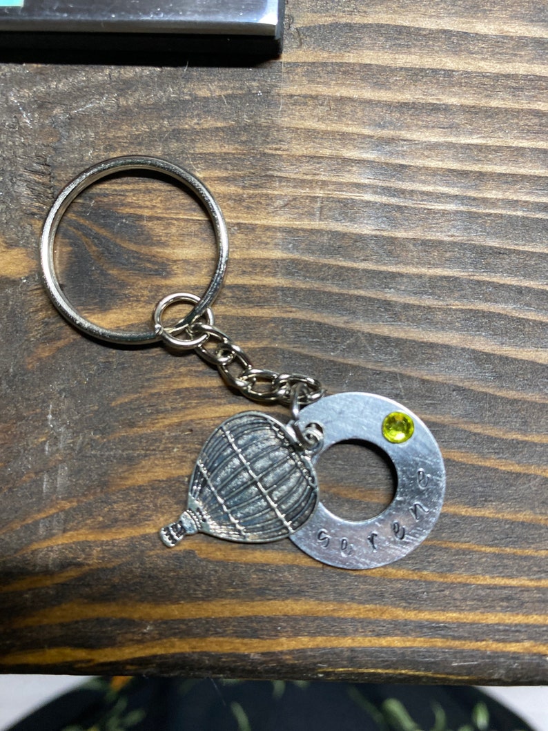Keychain with the word serene stamped on a washer with hot air balloon charm and green crystal.