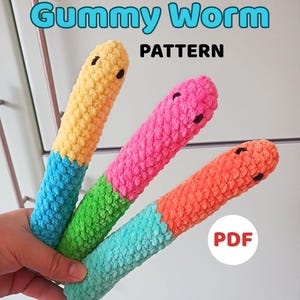 Puede incluir: Tres coloridos gusanos de goma de peluche en amarillo, rosa y naranja, cada uno con una base de diferente color. El texto "Gummy Worm PATTERN" está en la parte superior, y "PDF" en un círculo blanco en la parte inferior derecha.