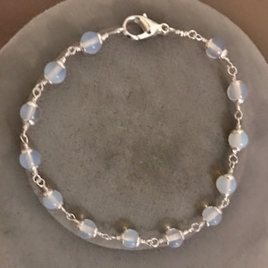 May include: A silver chain bracelet with light blue opal beads. The bracelet has a silver clasp.