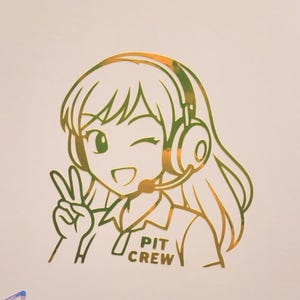 Könnte beinhalten: Ein holografischer Aufkleber mit einer Anime-Figur, die ein Headset trägt und ein Friedenszeichen macht. Die Figur hat langes Haar und trägt ein Hemd mit dem aufgedruckten Text PIT CREW. Ein kleines gelbes Grafiksymbol ist darüber zu sehen.