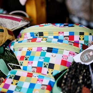 May include: A set of three colorful zippered pouches with a pixelated pattern featuring characters from the video game Minecraft. The pouches are made of a durable fabric and have a green zipper.