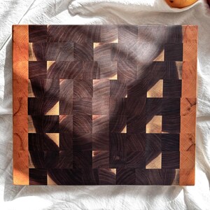 May include: A rectangular end-grain cutting board with a dark brown and tan checkerboard pattern. The edges are a lighter brown. The board is made of wood and is suitable for kitchen use.