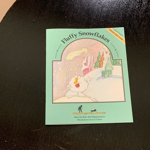May include: A green book cover with the title "Fluffy Snowflakes" in white text. The cover features a cartoon illustration of a snowman in a snowy landscape with houses in the background. The book is part of the "Steppingstone Stories" series.