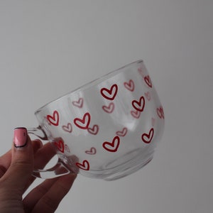K&ouml;nnte beinhalten: Eine klare Glas-Tasse mit einem roten Herz-Muster. Die Tasse hat einen Henkel und ist perfekt f&uuml;r hei&szlig;e Getr&auml;nke.
