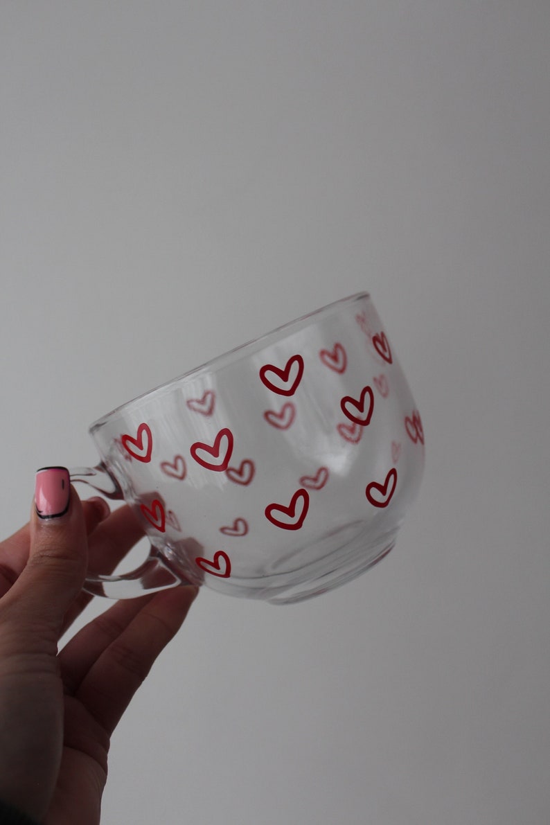 K&ouml;nnte beinhalten: Eine klare Glas-Tasse mit einem roten Herz-Muster. Die Tasse hat einen Henkel und ist perfekt f&uuml;r hei&szlig;e Getr&auml;nke.