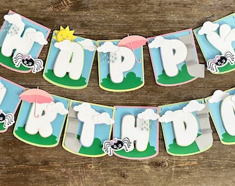 May include: A colorful banner spelling "HAPPY BIRTHDAY" with white letters, clouds, rain, suns, and spiders. Each letter is on a separate flag with a blue sky background, green grass, and a pink border. The banner is strung together.