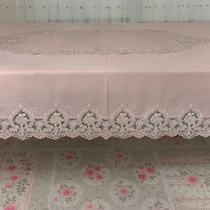Puede incluir: Un mantel de mesa rosa con un delicado borde de encaje. El mantel tiene un diseño de encaje circular en el centro.