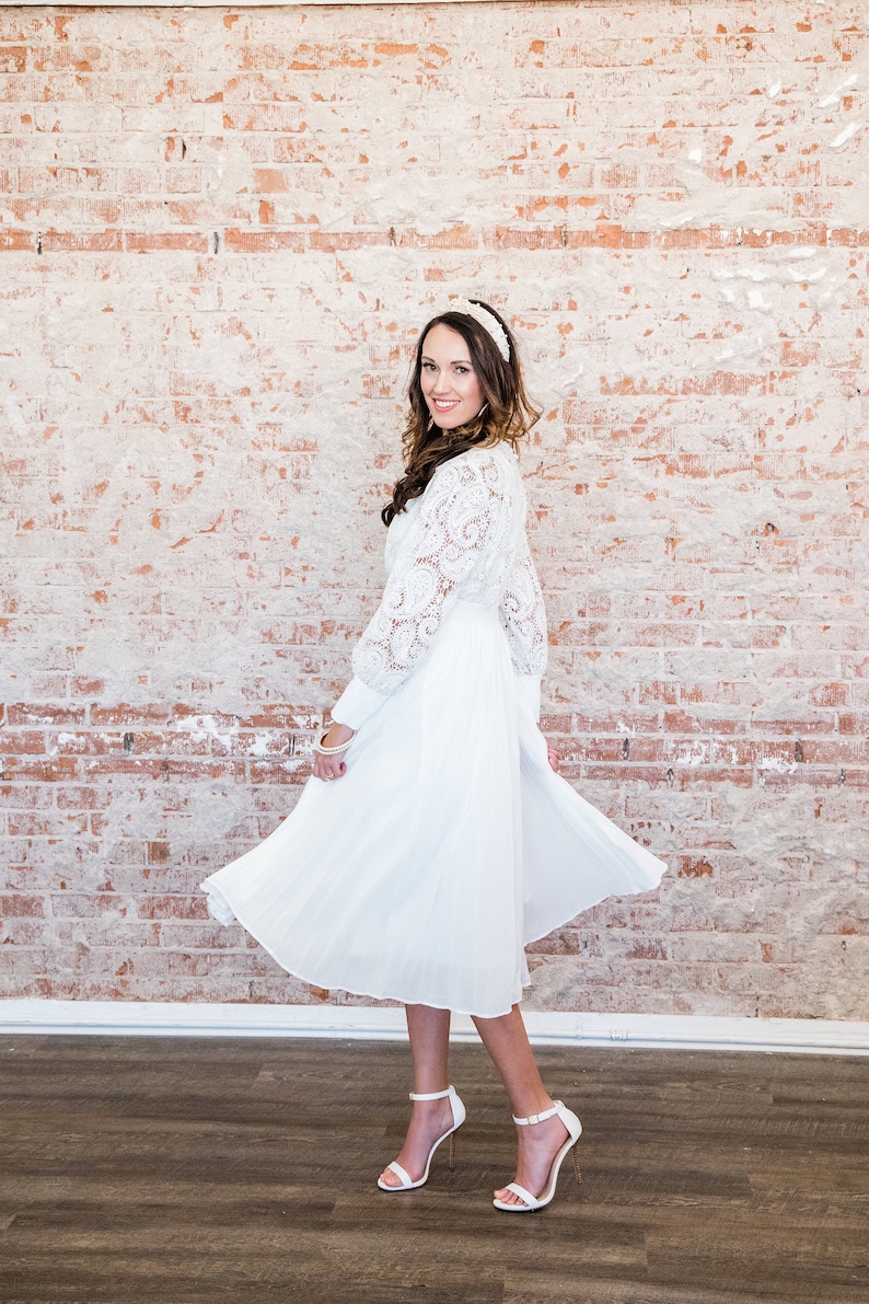 May include: A white lace dress with a white headband and white heels.
