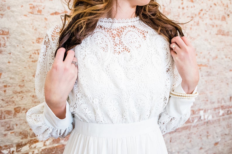 May include: A white lace dress with long sleeves and a high neckline.