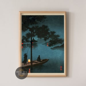 May include: A vintage Japanese woodblock print depicting a nighttime scene with two figures in a boat on a lake. The scene is illuminated by lanterns hanging from trees and buildings. The print is framed in a light wood frame.