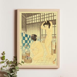 May include: A framed print of a Japanese woodblock print showing two nude figures in a bathhouse. The artwork uses a light colour palette with blue and white chequered tiles, wooden tubs, and architectural details.